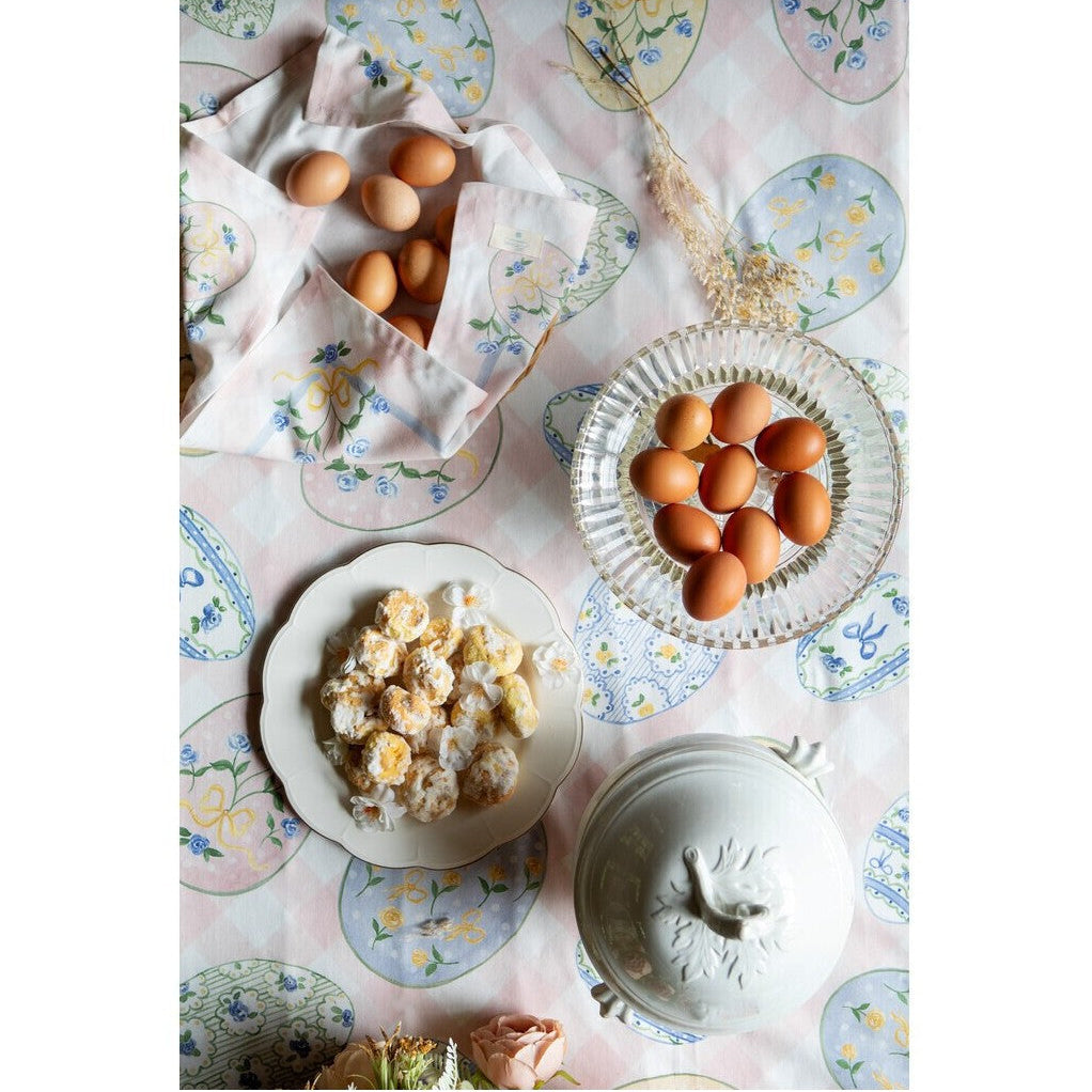 Tovaglia rettangolare della collezione "Pretty Easter" caratterizzata da una base a scacchi bianchi e rosa confetto con una balza in tinta unita sul bordo inferiore. Il tessuto è interamente stampato con uova di Pasqua decorate da motivi floreali, fiocchi gialli e trame geometriche nei toni del pastello, perfetta per apparecchiare la tavola festiva in stile shabby chic.