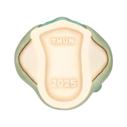 Statuina in ceramica Thun dell'Angelo della Natura Silvia, Limited Edition 2025, formato piccolo. L'angelo è raffigurato con gli occhi chiusi, ali verdi e una corona di foglie; indossa una veste color crema con bordi verdi e tiene tra le braccia, stringendolo al petto, un piccolo cerbiatto marrone. Design iconico Thun con finitura opaca e colori sfumati.