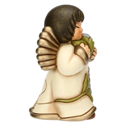 Statuina in ceramica Thun dell'Angelo dei Nonni Anna, collezione 2025. L'angelo è raffigurato con gli occhi chiusi, ali dorate e capelli castani. Indossa una veste color crema con bordi dorati e decorazioni floreali azzurre sulla parte inferiore. L'angelo tiene tra le mani un mazzo di fiori azzurri con foglie verdi, portandoli vicino al viso. Design classico Thun con finitura lucida e forme arrotondate.