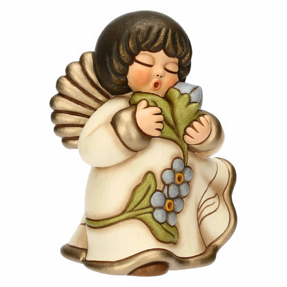 Statuina in ceramica Thun dell'Angelo dei Nonni Anna, collezione 2025. L'angelo è raffigurato con gli occhi chiusi, ali dorate e capelli castani. Indossa una veste color crema con bordi dorati e decorazioni floreali azzurre sulla parte inferiore. L'angelo tiene tra le mani un mazzo di fiori azzurri con foglie verdi, portandoli vicino al viso. Design classico Thun con finitura lucida e forme arrotondate.