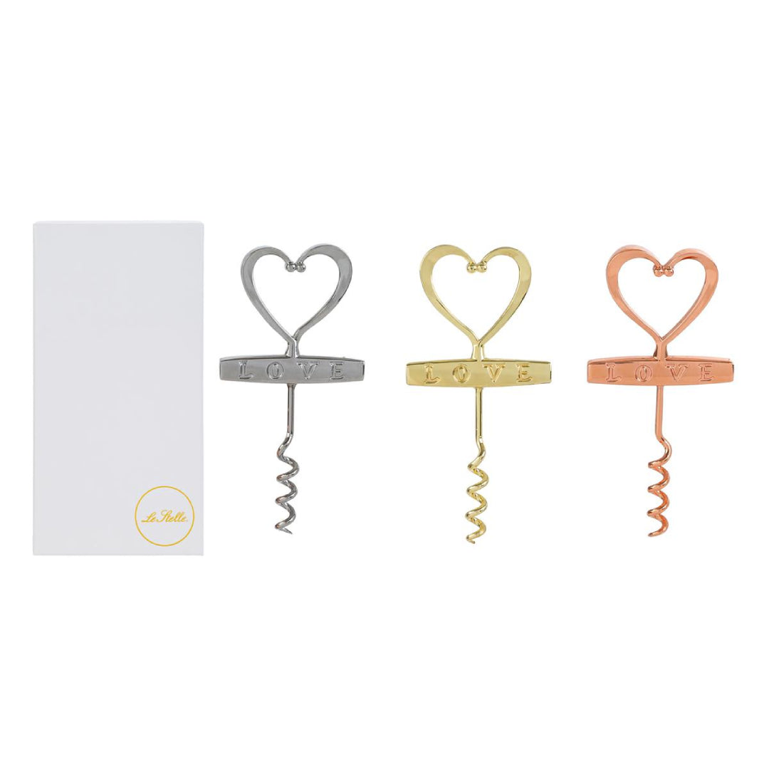 Cavatappi in metallo a forma di cuore con scritta "Love" incisa, disponibile in tre finiture assortite argento, oro e rosé, presentato accanto alla sua confezione bianca con logo "Le Stelle". Accessorio da tavola originale ideale come bomboniera o idea regalo per matrimoni ed eventi.