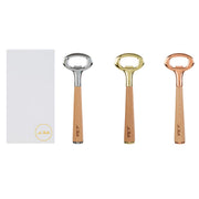 Apribottiglie con manico in legno chiaro inciso "Le Stelle" e testa in metallo, disponibile in tre finiture assortite argento, oro e rosé, presentato accanto alla sua confezione bianca con logo del marchio. Utensile da cucina elegante e funzionale, ideale come bomboniera o idea regalo raffinata.