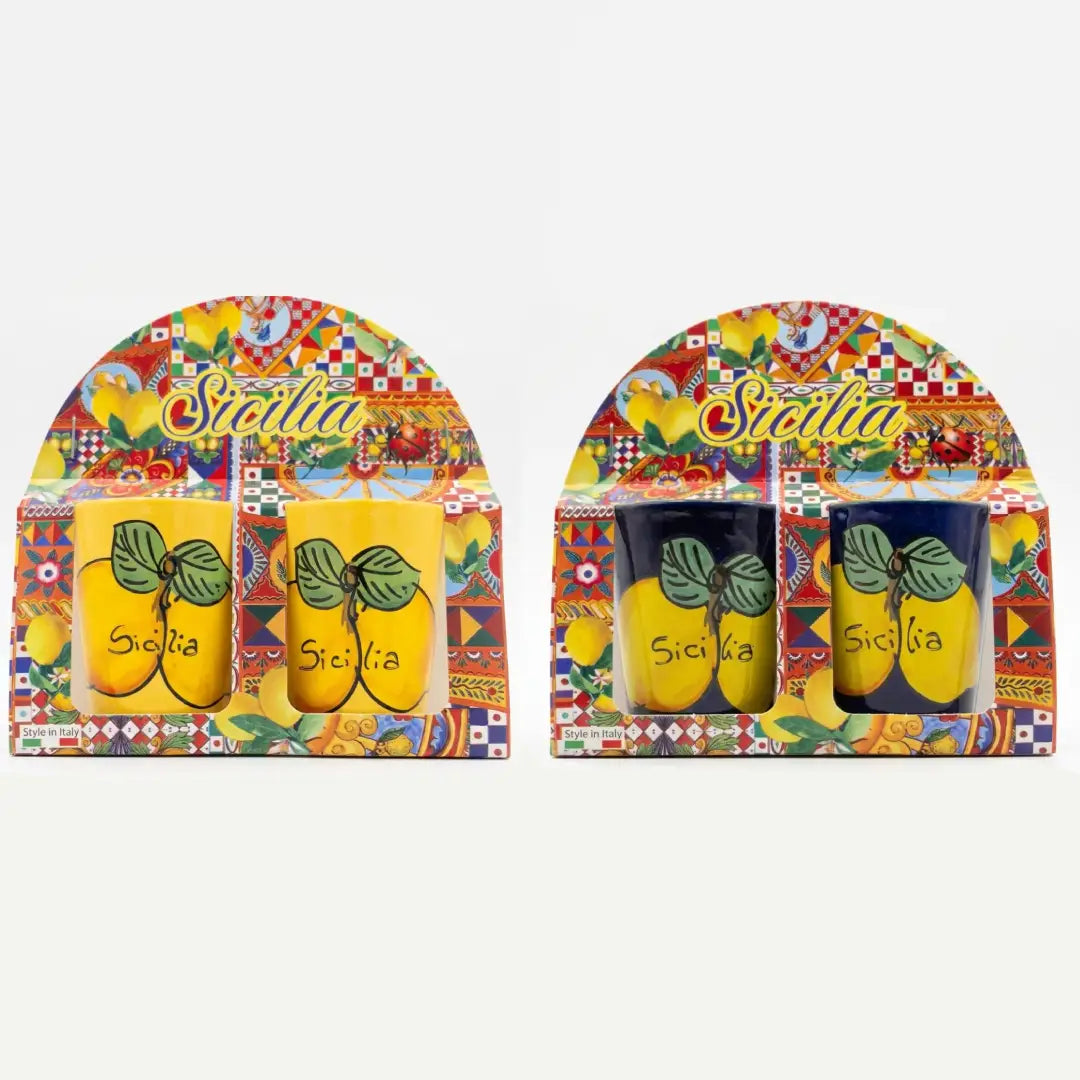 Coppia di bicchierini in ceramica decorati con vivaci limoni e la scritta "Sicilia" su sfondo blu scuro o giallo brillante, perfetti per servire liquori come il limoncello. Questa coppia di tazzine artigianali si presenta in una confezione regalo assortita in stile maiolica siciliana, ideale come souvenir colorato o come bomboniera per eventi speciali.