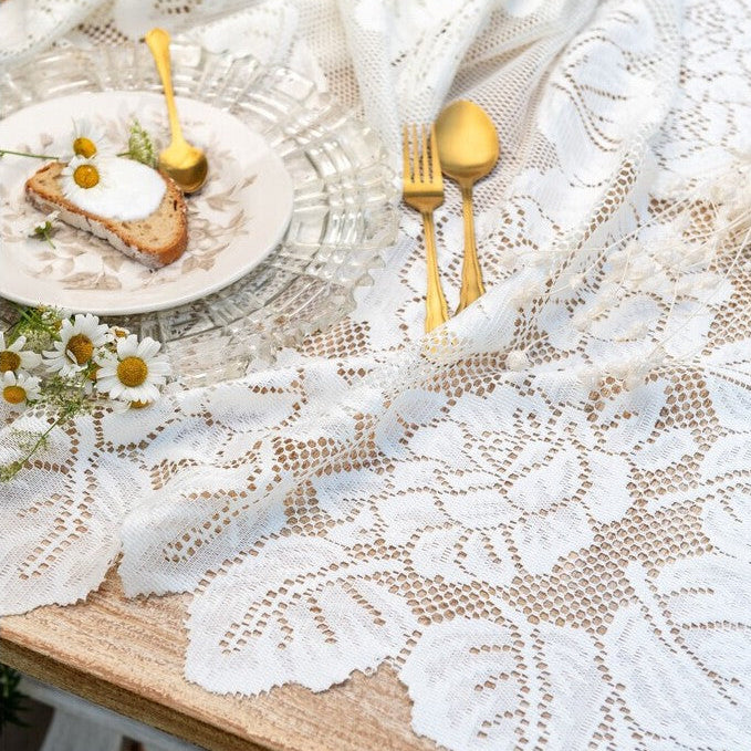 Tovaglia in pizzo bianco della collezione "Dentelle" di Blanc Mariclo' adatta per impreziosire la tavola con uno stile shabby chic ed elegante. Il dettaglio mostra due varianti assortite di tovaglie ricamate con motivi floreali e bordi smerlati ideali per la cucina o il soggiorno.