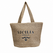 Borsa di paglia intrecciata color naturale con manici lunghi, decorata sul davanti con la scritta ricamata "Sicilia Italia" e un piccolo stemma araldico ricamato in blu scuro. Borsa mare in paglia stile artigianale, ideale come accessorio estivo o souvenir siciliano, dal design capiente e informa a shopper.