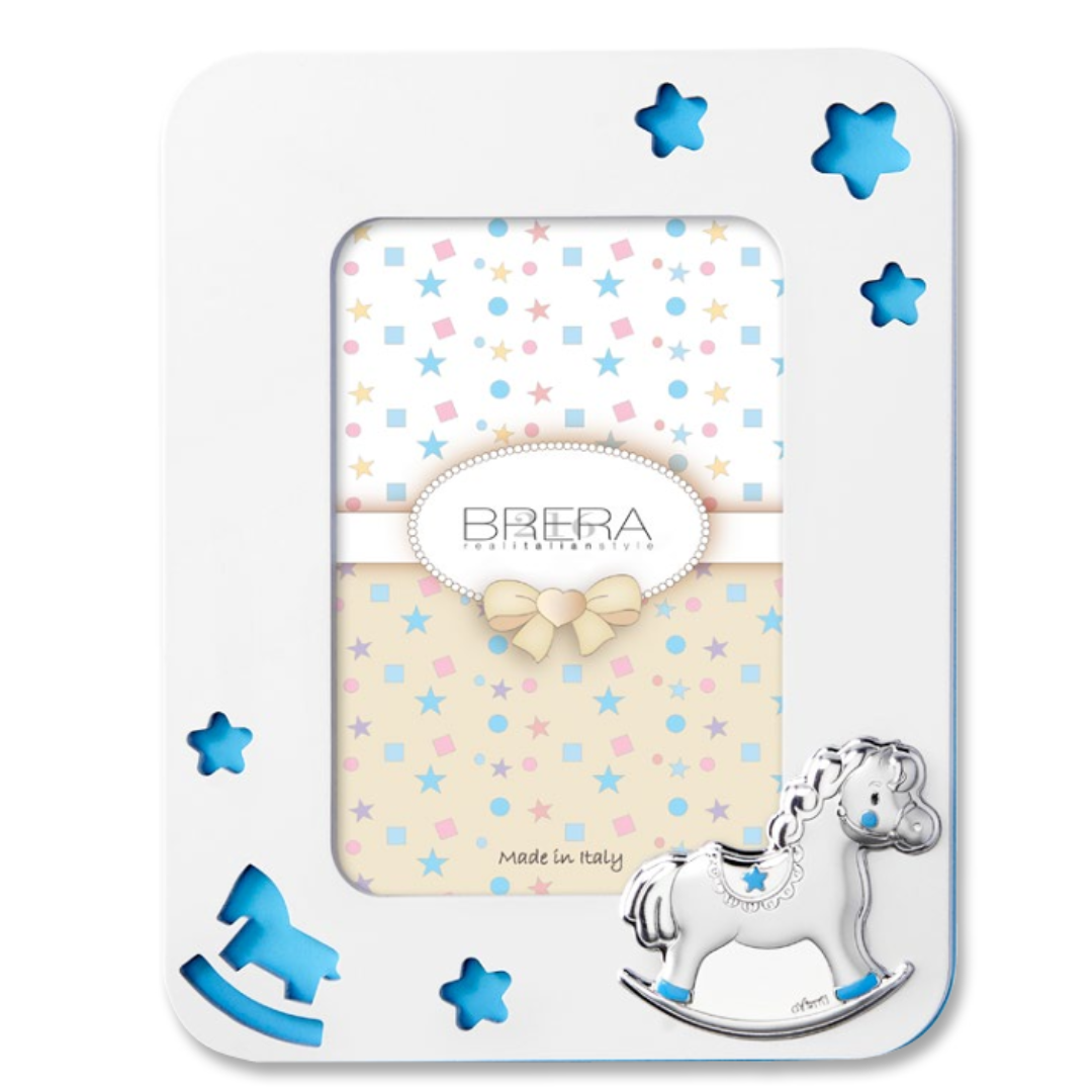 Portafoto per bambina in legno bianco con cornice sagomata e angoli arrotondati. Presenta trafori a forma di stelle e di un cavallino a dondolo che rivelano uno sfondo celeste pastello. In basso a destra è applicato un cavallino a dondolo in argento bilaminato con dettagli rosa sulle zampe e sulla sella. L'interno mostra un inserto decorativo con stelle e il logo "Brera - Real Italian Style".