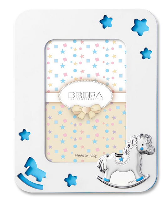 Portafoto per bambina in legno bianco con cornice sagomata e angoli arrotondati. Presenta trafori a forma di stelle e di un cavallino a dondolo che rivelano uno sfondo celeste pastello. In basso a destra è applicato un cavallino a dondolo in argento bilaminato con dettagli rosa sulle zampe e sulla sella. L'interno mostra un inserto decorativo con stelle e il logo "Brera - Real Italian Style".