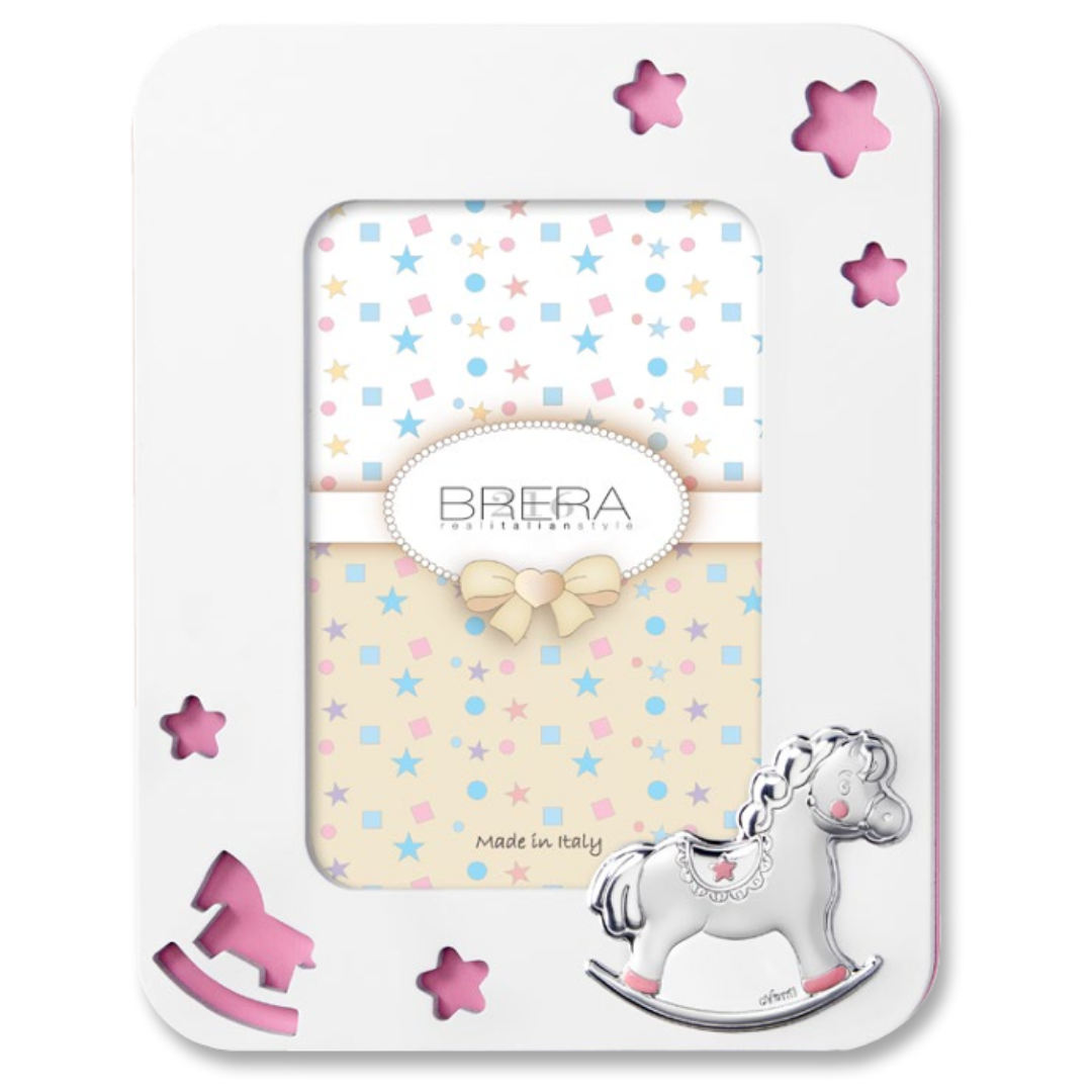 Portafoto per bambina in legno bianco con cornice sagomata e angoli arrotondati. Presenta trafori a forma di stelle e di un cavallino a dondolo che rivelano uno sfondo rosa pastello. In basso a destra è applicato un cavallino a dondolo in argento bilaminato con dettagli rosa sulle zampe e sulla sella. L'interno mostra un inserto decorativo con stelle e il logo "Brera - Real Italian Style".