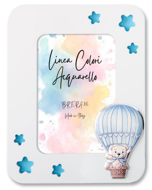 Portafoto da tavolo per bambino con cornice in legno bianco. L'angolo in basso a destra è decorato con un'applicazione smaltata in rilievo che raffigura un dolce orsetto seduto nel cestino di una mongolfiera a strisce celeste e panna. All'interno è presente l'inserto "Linea Colori Acquarello - Brera 216 - Made in Italy" su sfondo sfumato pastello.