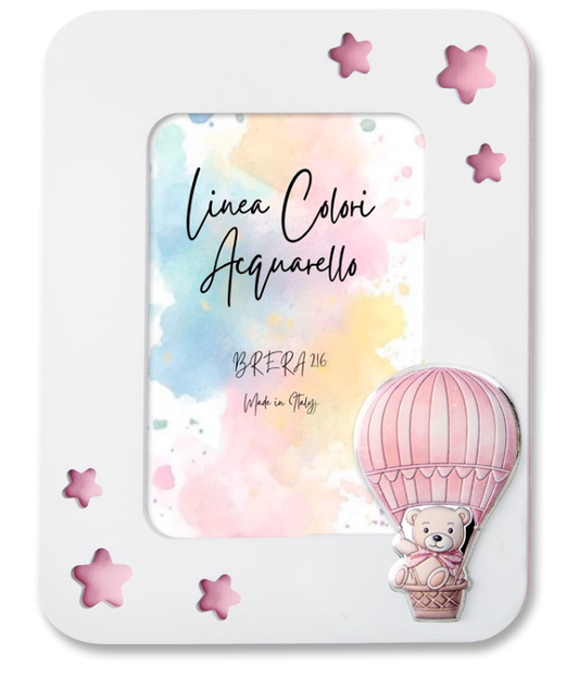 Portafoto da tavolo per bambina con cornice in legno bianco. L'angolo in basso a destra è decorato con un'applicazione smaltata in rilievo che raffigura un dolce orsetto seduto nel cestino di una mongolfiera a strisce rosa e panna. All'interno è presente l'inserto "Linea Colori Acquarello - Brera 216 - Made in Italy" su sfondo sfumato pastello.