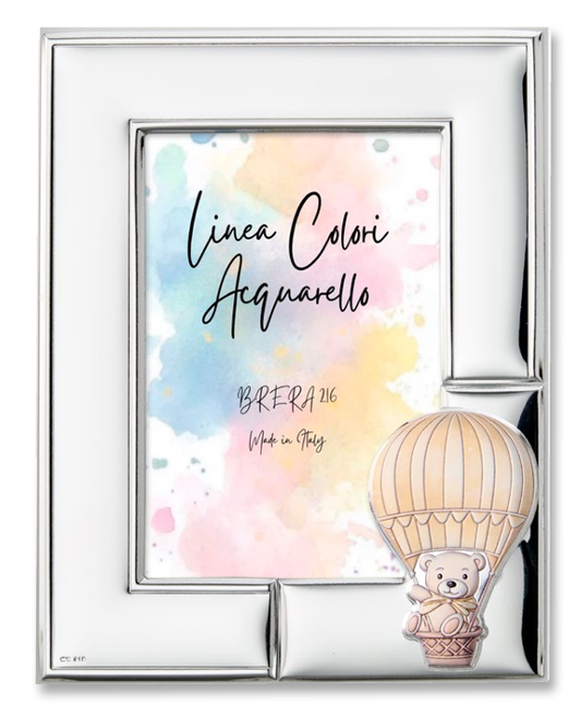 Portafoto da tavolo per bambini con cornice in argento bilaminato lucido. L'angolo in basso a destra è decorato con un'applicazione smaltata in rilievo che raffigura un dolce orsetto seduto nel cestino di una mongolfiera a strisce beige e panna. All'interno è presente l'inserto "Linea Colori Acquarello - Brera 216 - Made in Italy" su sfondo sfumato pastello.