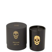 Candela profumata "Cranio" Nuit Noire firmata Jolipa, caratterizzata da un elegante bicchiere in vetro nero lucido impreziosito da un teschio dorato in rilievo sulla parte frontale. Questa esclusiva candela decorativa di lusso è accompagnata dalla sua confezione regalo cilindrica coordinata total black con dettagli in oro, ideale per profumare la casa e creare un'atmosfera moderna, audace e sofisticata.
