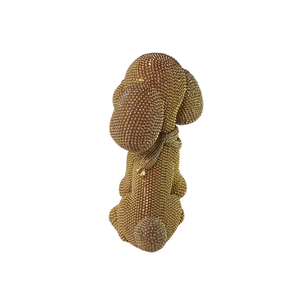 Statuina in resina raffigurante un cagnolino dorato seduto con lunghe orecchie pendenti e una sciarpa arrotolata al collo, interamente ricoperto di brillantini glitterati, con occhi e naso neri. Oggetto decorativo scintillante firmato Sud Import, ideale come soprammobile per bambini o idea regalo per gli amanti degli animali.