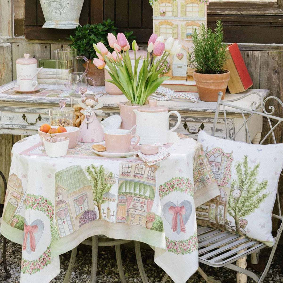 ambientazione del centrotavola Nuvole di Stoffa linea "La Vie en Rose" con illustrazioni di negozi parigini e pasticcerie vintage. Decorazione con ghirlande di rose, cuori azzurri con fiocchi rosa e farfalle su fondo bianco.