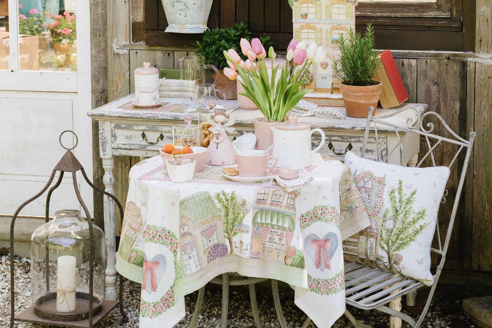 ambientazione del centrotavola Nuvole di Stoffa linea "La Vie en Rose" con illustrazioni di negozi parigini e pasticcerie vintage. Decorazione con ghirlande di rose, cuori azzurri con fiocchi rosa e farfalle su fondo bianco.