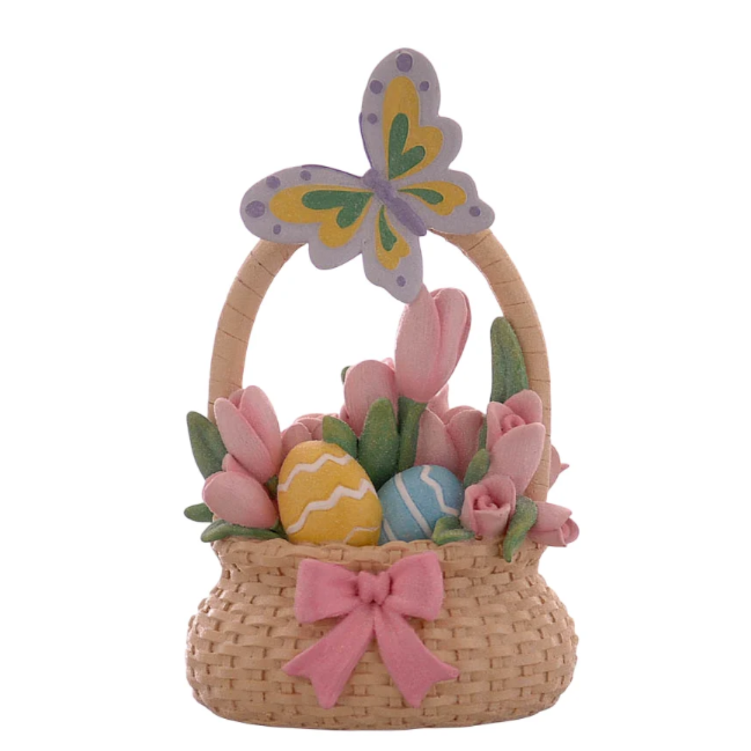Statuina decorativa in resina raffigurante un cestino intrecciato color sabbia con un grande fiocco rosa sul davanti. Il cestino è colmo di tulipani rosa e uova di Pasqua decorate (una gialla e una azzurra con motivi a zig-zag). Sul manico del cestino è posata una grande farfalla colorata con ali lilla, gialle e verdi.