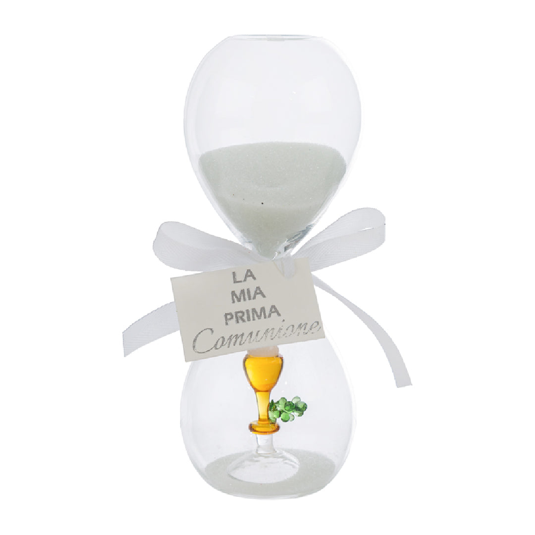 Clessidra in vetro trasparente riempita di sabbia bianca, con un calice dorato e un rametto verde all'interno del bulbo inferiore e fiocco bianco con etichetta "La mia prima Comunione". Bomboniera decorativa presentata con la sua confezione bianca del marchio Le Stelle, ideale come ricordo per la Prima Comunione.