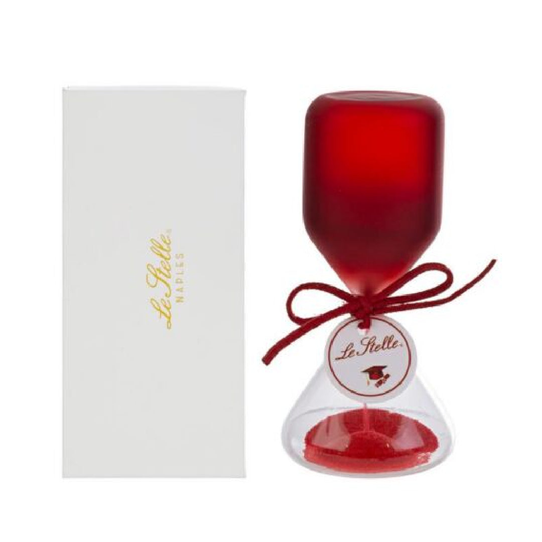 Clessidra in vetro satinato rosso a forma di clava, con base conica trasparente riempita di sabbia rossa e cordoncino con etichetta tonda "Le Stelle" decorata da un cappello di laurea. Oggetto decorativo elegante presentato con la sua confezione bianca del marchio, ideale come bomboniera per lauree o idea regalo raffinata.