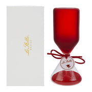 Clessidra in vetro satinato rosso a forma di clava, con base conica trasparente riempita di sabbia rossa e cordoncino con etichetta tonda "Le Stelle" decorata da un cappello di laurea. Oggetto decorativo elegante presentato con la sua confezione bianca del marchio, ideale come bomboniera per lauree o idea regalo raffinata.