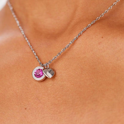 Primo piano della collana Lucky Light indossata. La catena d'acciaio poggia delicatamente sul décolleté, mettendo in risalto i pendenti con cristallo fucsia e il cuore in acciaio lucido.