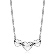 Collana in acciaio lucido con maglia a serpente e tre pendenti a forma di cuore bombato scorrevoli. I cuori specchiati degradano leggermente in dimensione, con il più grande posto al centro.
