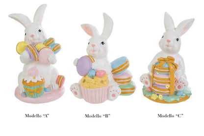 Tris di statuine pasquali assortite del marchio Le Stelle (codice 12244) raffiguranti coniglietti bianchi con dolci e pasticcini. Il Modello A tiene dei macaron e ha un cupcake alla base; il Modello B è seduto accanto a una pila di macaron e un grande pasticcino; il Modello C tiene una torre di macaron legata con un fiocco dorato. Decorazioni in resina dai colori pastello.
