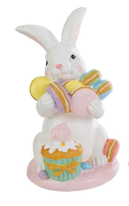Tris di statuine pasquali assortite del marchio Le Stelle (codice 12244) raffiguranti coniglietti bianchi con dolci e pasticcini. Il Modello A tiene dei macaron e ha un cupcake alla base; il Modello B è seduto accanto a una pila di macaron e un grande pasticcino; il Modello C tiene una torre di macaron legata con un fiocco dorato. Decorazioni in resina dai colori pastello.