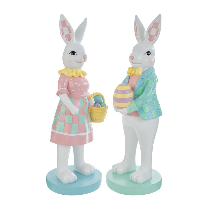 Coppia di statuine decorative a forma di conigli bianchi in piedi su basi circolari color pastello. La coniglietta indossa un abito rosa a pois con gonna a scacchi verdi e tiene un cestino di uova; il coniglio indossa una giacca a scacchi azzurri e verdi con papillon giallo e regge un uovo decorato. Design in stile MacKenzie-Childs per il marchio Le Stelle.