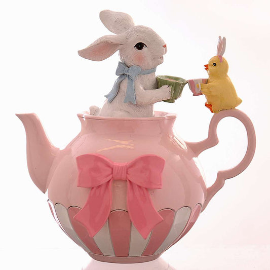 Decorazione pasquale Vetur in poliresina. Scenetta con coniglietto bianco con fiocco azzurro all'interno di una teiera rosa a righe con fiocco fucsia, mentre offre il tè a un piccolo pulcino. Altezza 20 cm.