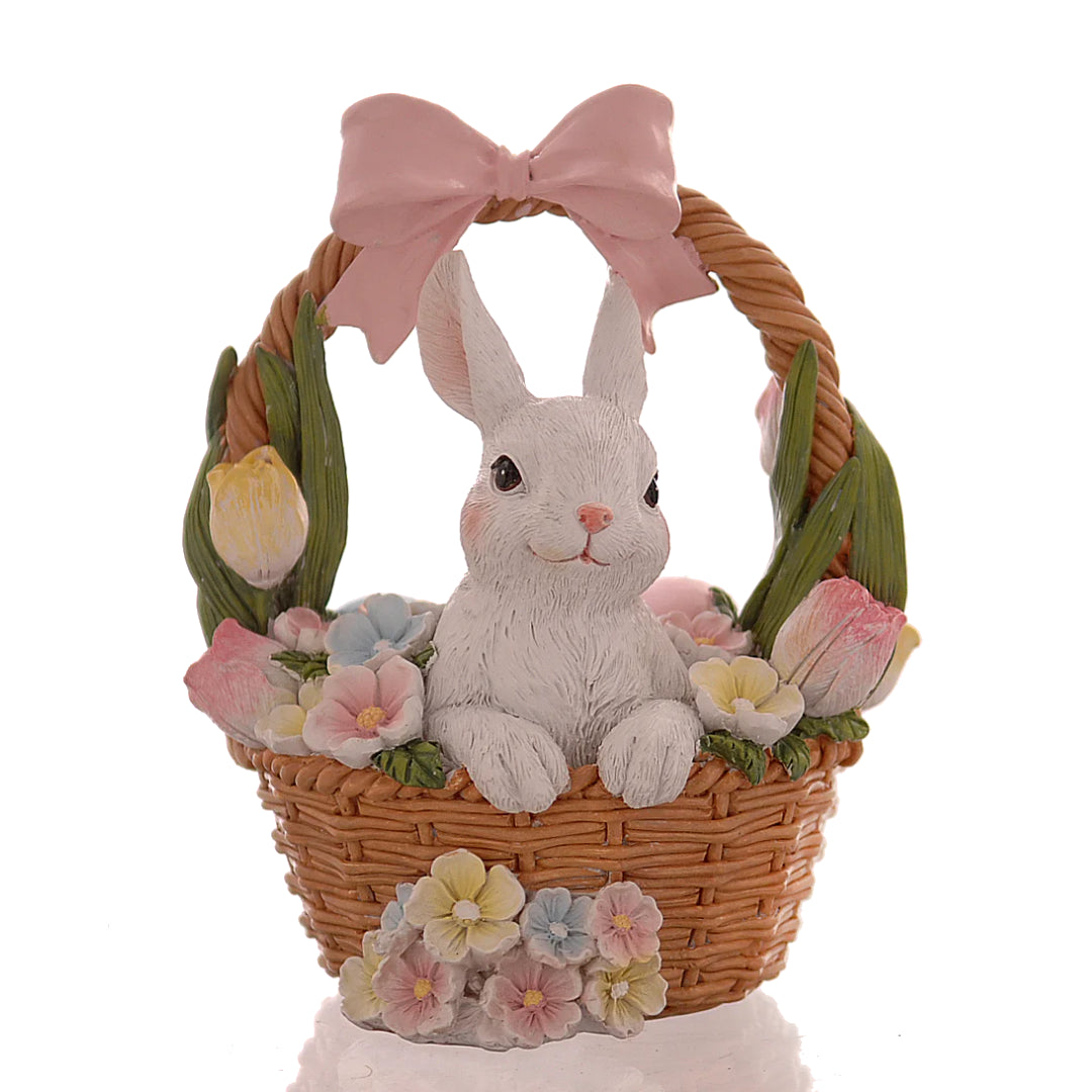 Decorazione pasquale Vetur in poliresina. Coniglietto bianco seduto all'interno di un cestino di vimini intrecciato, circondato da tulipani e fiori primaverili pastello, con un grande fiocco rosa sul manico.