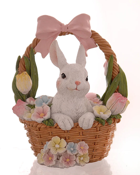 Decorazione pasquale Vetur in poliresina. Coniglietto bianco seduto all'interno di un cestino di vimini intrecciato, circondato da tulipani e fiori primaverili pastello, con un grande fiocco rosa sul manico.