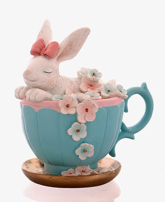 Decorazione pasquale scultorea Vetur in poliresina. Coniglietto bianco con fiocco rosaseduto all'interno di una tazza da tè azzurra decorata con fiori rosa e celesti sfumati, appoggiata su un piattino dorato.