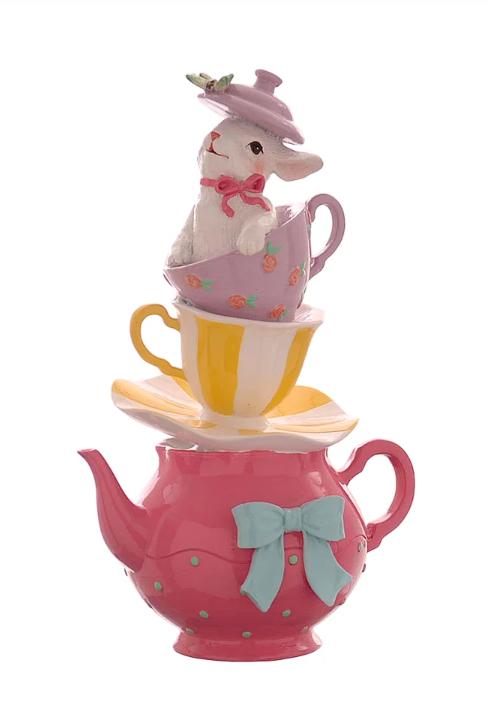 Statuina decorativa in resina raffigurante una torre composta da una teiera fucsia a pois verdi con fiocco azzurro, un piattino ondulato giallo e bianco, una tazzina gialla a righe e una tazzina lilla decorata con rose. In cima, un coniglietto bianco sbuca dalla tazzina indossando il coperchio lilla della teiera come un cappello. Design verticale in stile Alice nel Paese delle Meraviglie.