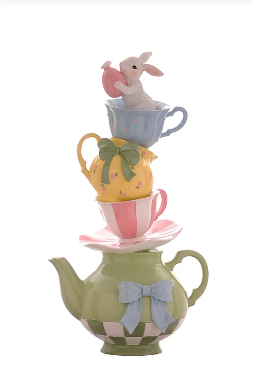 Statuina decorativa in resina composta da una torre di stoviglie multicolor: alla base una teiera verde con fiocco azzurro, sormontata da un piattino, una tazzina a righe rosa, una brocca gialla con fiocco verde e una tazzina azzurra a pois. In cima, un coniglietto bianco sbuca dalla tazzina tenendo tra le zampe un uovo di Pasqua rosa. Design verticale dai colori pastello.