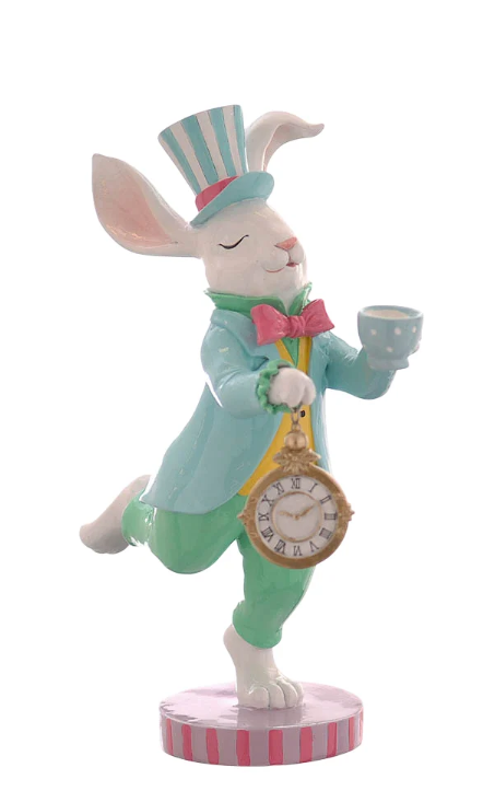 Statuina decorativa in resina di un coniglio bianco antropomorfo in posa dinamica su una zampa sola. Il coniglio indossa un cappello a cilindro a righe bianche e azzurre, una giacca azzurra, un gilet giallo con papillon rosa e pantaloni verdi. Tiene in mano una tazzina da tè azzurra a pois e un grande orologio da taschino dorato. Base circolare a righe rosa e lilla.