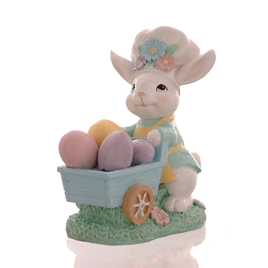 Decorazione pasquale Vetur in poliresina h 16 cm. Personaggio coniglio bianco vestito con giacca azzurra e pantaloni verdi che trasporta una pila di uova di Pasqua colorate e decorate con fiori.
