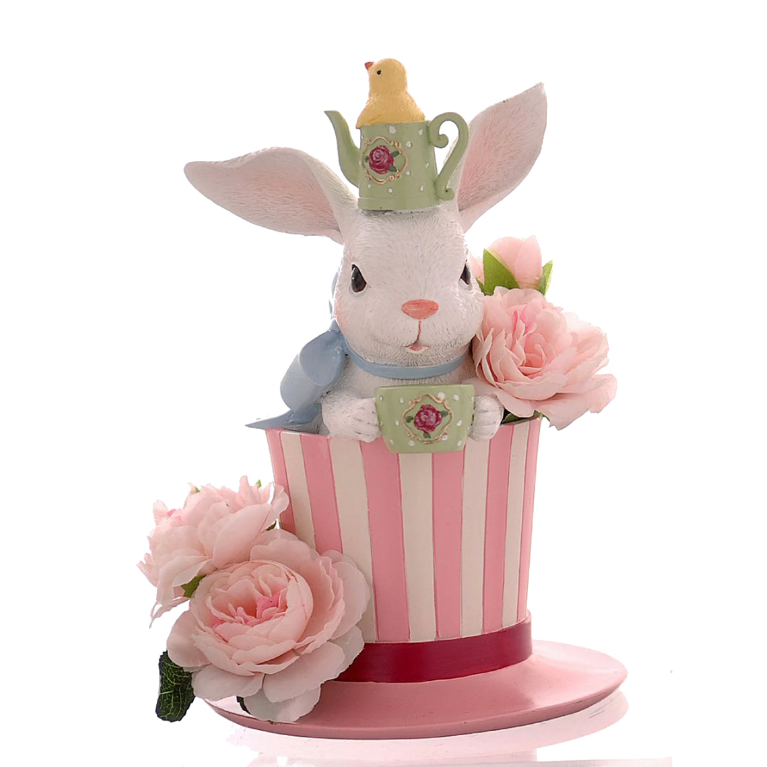 Decorazione pasquale scultorea Vetur in poliresina. Coniglio bianco che spunta da un cappello a cilindro a righe bianche e rosa, con indosso una mini teiera verde come cappellino e grandi rose rosa decorative alla base.