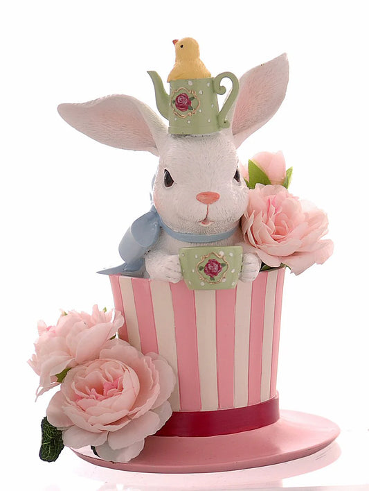 Decorazione pasquale scultorea Vetur in poliresina. Coniglio bianco che spunta da un cappello a cilindro a righe bianche e rosa, con indosso una mini teiera verde come cappellino e grandi rose rosa decorative alla base.