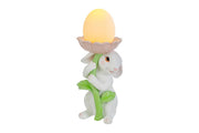 Statuina pasquale del marchio Le Stelle raffigurante un coniglietto bianco che abbraccia lo stelo verde di un grande fiore rosa. All'interno della corolla del fiore è posizionato un uovo luminoso a LED giallo che funge da lampada. Decorazione in resina per Pasqua 2026 con finitura dettagliata e colori pastello.
