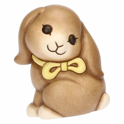 Statuina in ceramica Thun raffigurante il coniglio Roger della collezione Incanto di Pasqua. Il coniglietto, nei classici toni del marrone sfumato, è ritratto seduto con un fiocco giallo al collo e grandi occhi dolci. Iconica decorazione pasquale Thun con finitura opaca e forme morbide.