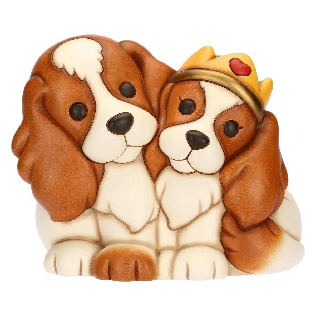 Statuina in ceramica Thun raffigurante una coppia di cani Cavalier King accovacciati uno accanto all'altro. Sono dipinti nei toni del bianco e del marrone caldo; il cane a destra indossa una corona dorata decorata con un piccolo cuore rosso. Lo stile è quello classico e tondeggiante tipico del brand.