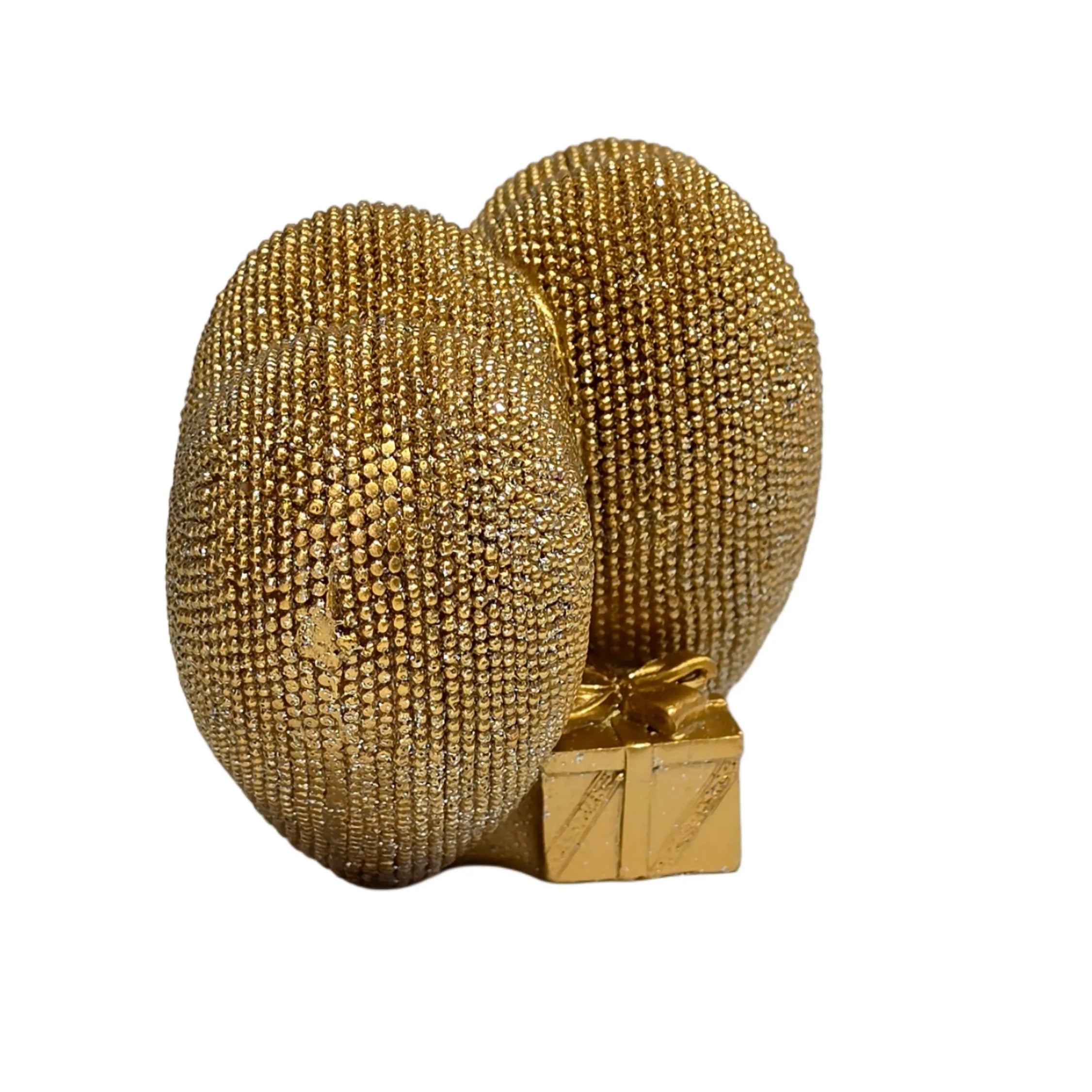 Statuina in resina raffigurante due cuori dorati affiancati, interamente ricoperti di brillantini glitterati, con un piccolo pacco regalo dorato liscio incastonato alla base. Oggetto decorativo firmato Sud Import, ideale come soprammobile romantico o idea regalo per San Valentino e occasioni speciali.