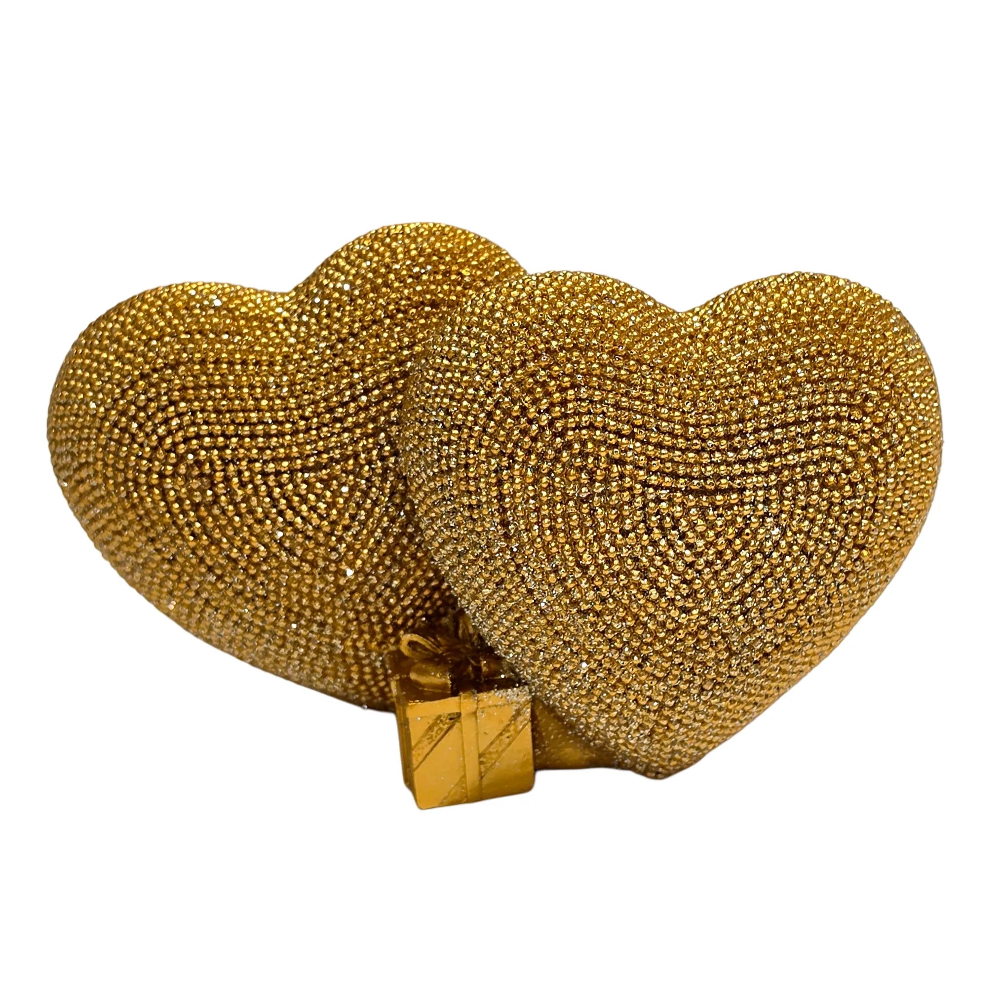 Statuina in resina raffigurante due cuori dorati affiancati, interamente ricoperti di brillantini glitterati, con un piccolo pacco regalo dorato liscio incastonato alla base. Oggetto decorativo firmato Sud Import, ideale come soprammobile romantico o idea regalo per San Valentino e occasioni speciali.
