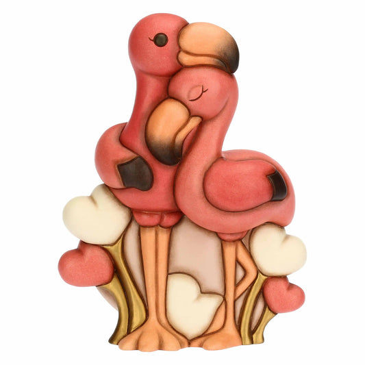 Statua maxi in ceramica raffigurante una coppia di fenicotteri rosa abbracciati. Alla base, cuori bianchi e rosa tra fili d'erba dorati. Design stilizzato con finitura opaca e dettagli caldi. Vista frontale.