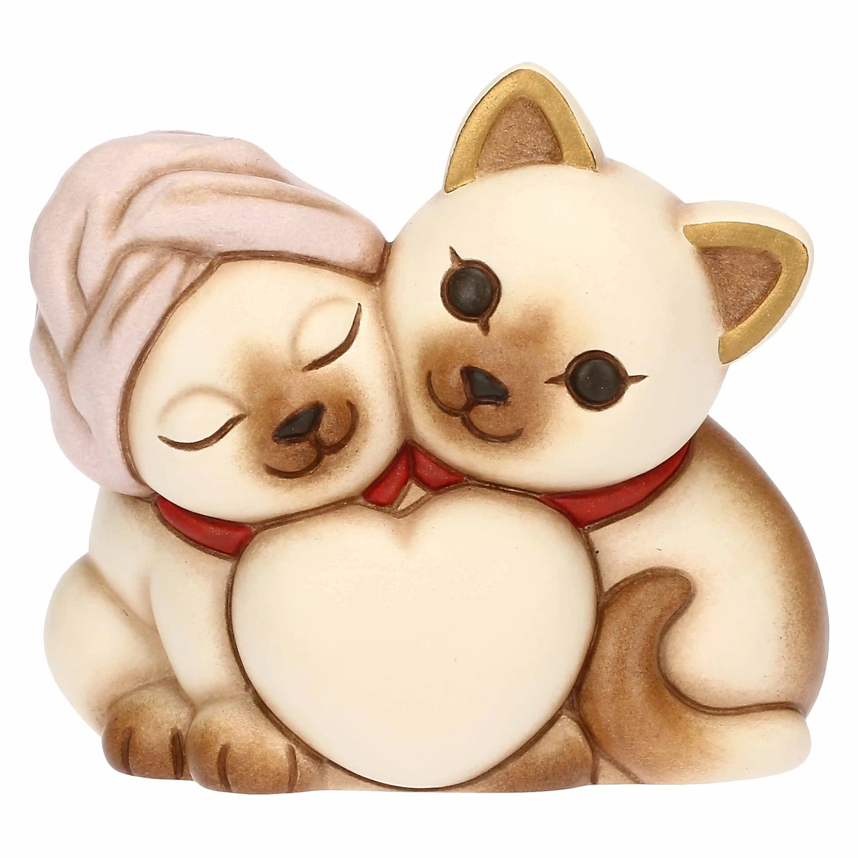 L'immagine mostra una statuetta decorativa in ceramica dallo stile dolce e arrotondato, raffigurante una coppia di gattini siamesi abbracciati dietro un grande cuore bianco centrale.