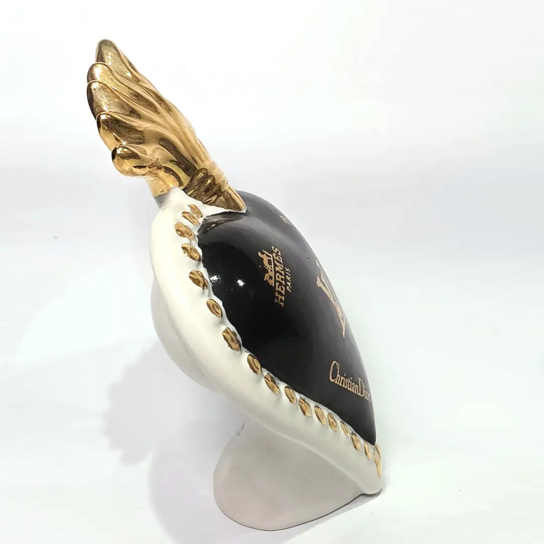 Scultura in ceramica a forma di Cuore Sacro firmata Sbordone, caratterizzata da un corpo nero lucido decorato con loghi fashion dorati e una fiamma superiore in oro. L'opera è rifinita da una cornice bianca perlinata con borchie dorate, rappresentando un complemento d'arredo pop art esclusivo e moderno per interni di design.