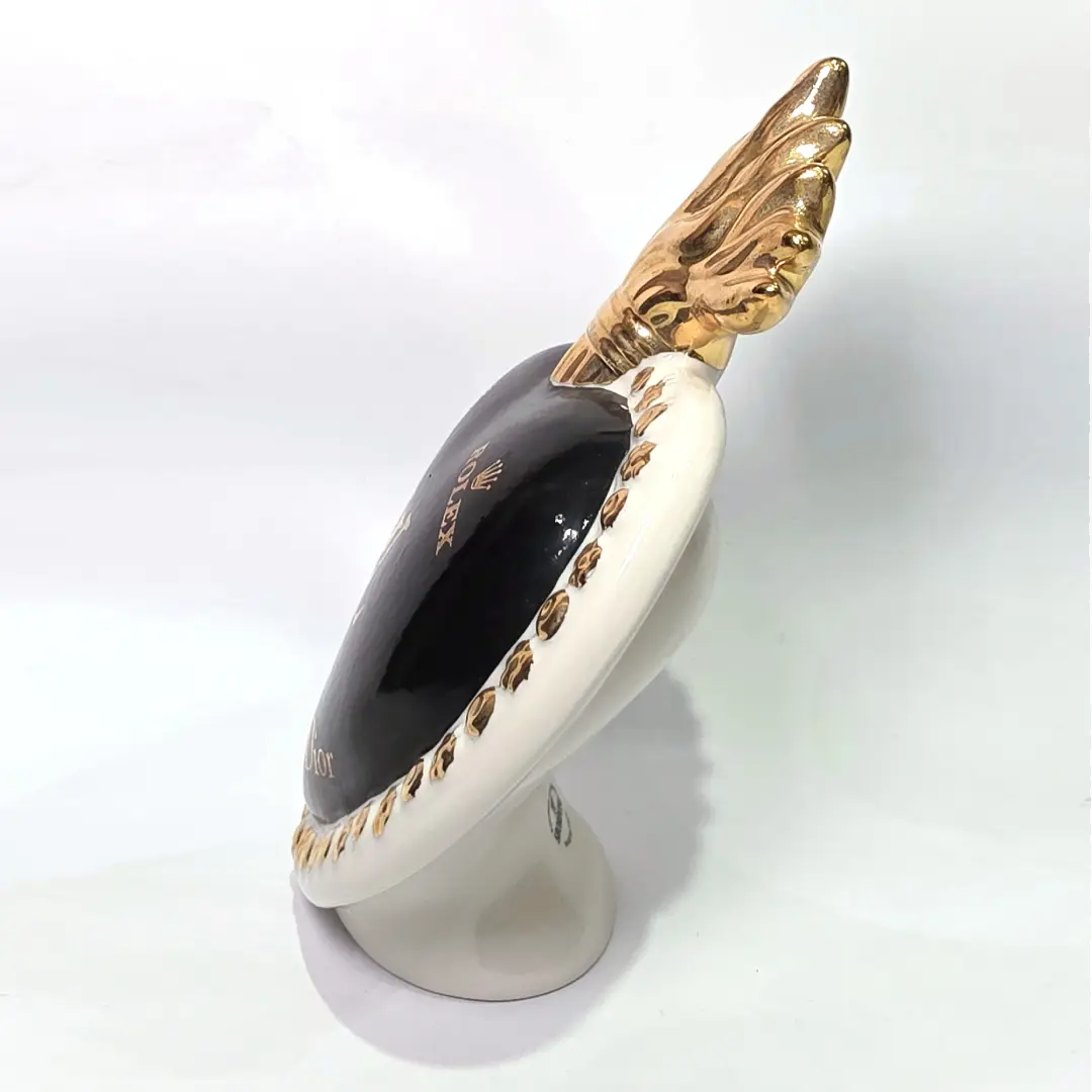 Scultura in ceramica a forma di Cuore Sacro firmata Sbordone, caratterizzata da un corpo nero lucido decorato con loghi fashion dorati e una fiamma superiore in oro. L'opera è rifinita da una cornice bianca perlinata con borchie dorate, rappresentando un complemento d'arredo pop art esclusivo e moderno per interni di design.
