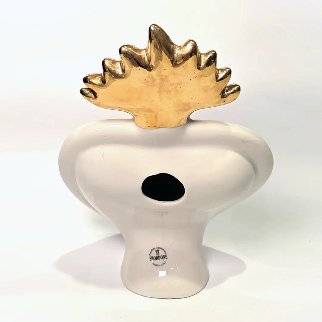 Scultura in ceramica a forma di Cuore Sacro firmata Sbordone, caratterizzata da un corpo nero lucido decorato con loghi fashion dorati e una fiamma superiore in oro. L'opera è rifinita da una cornice bianca perlinata con borchie dorate, rappresentando un complemento d'arredo pop art esclusivo e moderno per interni di design.