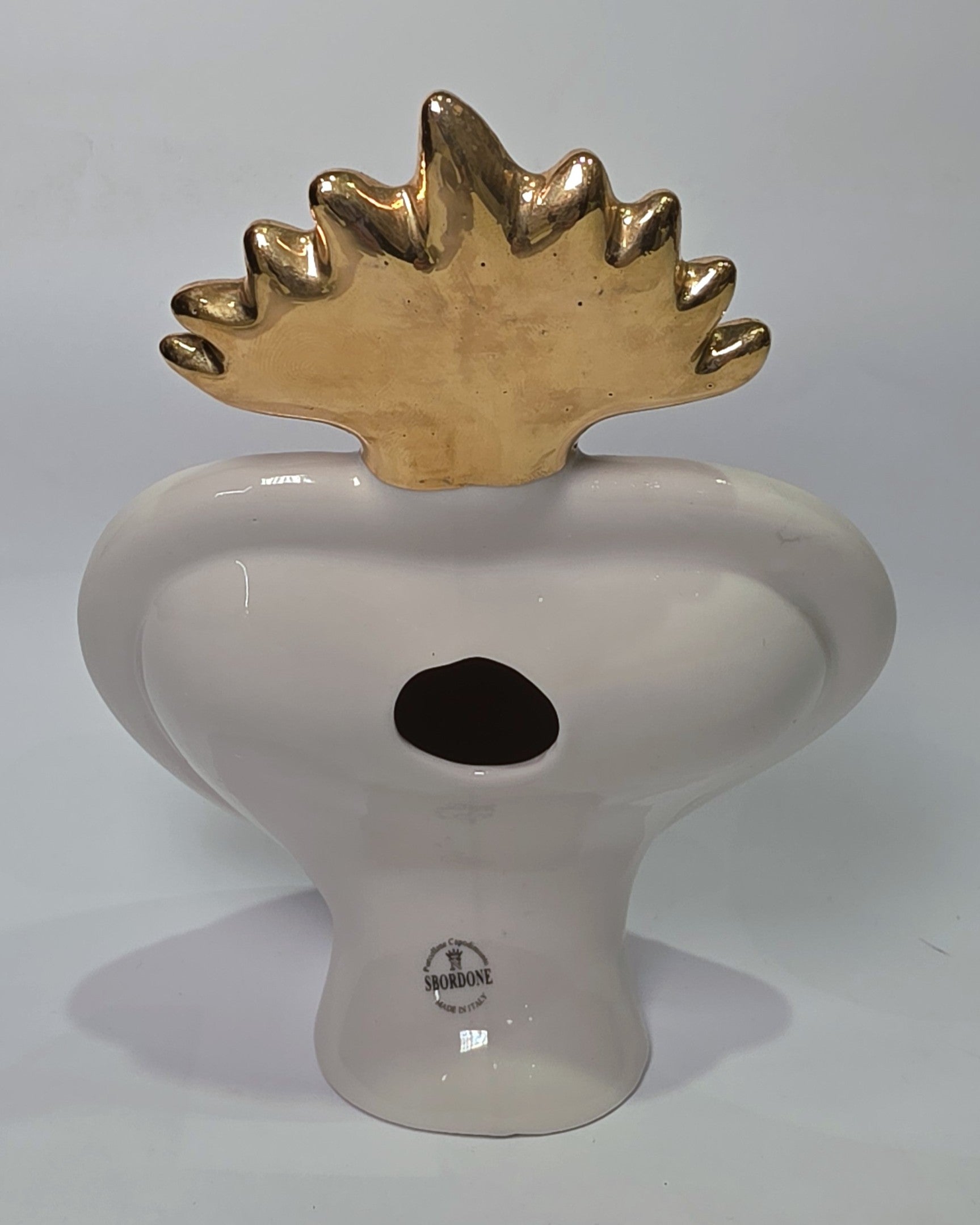 Scultura in ceramica a forma di Cuore Sacro firmata Sbordone, caratterizzata da un corpo nero lucido decorato con loghi fashion dorati e una fiamma superiore in oro. L'opera è rifinita da una cornice bianca perlinata con borchie dorate, rappresentando un complemento d'arredo pop art esclusivo e moderno per interni di design.