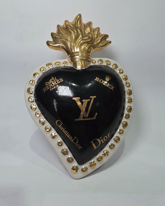 Scultura in ceramica a forma di Cuore Sacro firmata Sbordone, caratterizzata da un corpo nero lucido decorato con loghi fashion dorati e una fiamma superiore in oro. L'opera è rifinita da una cornice bianca perlinata con borchie dorate, rappresentando un complemento d'arredo pop art esclusivo e moderno per interni di design.